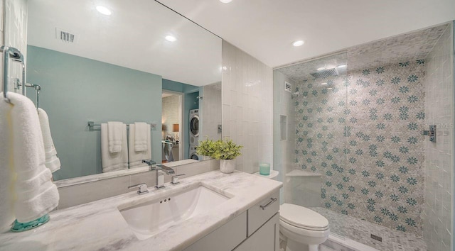 bathroom with stacked washer and dryer, vanity, tiled shower, and toilet