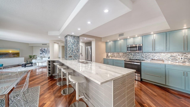 kitchen with a large island with sink, appliances with stainless steel finishes, sink, and light stone counters