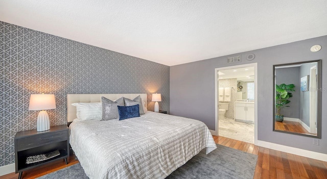 bedroom with wood-type flooring, connected bathroom, and a textured ceiling