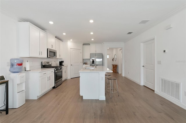 kitchen with stainless steel appliances, white cabinetry, light hardwood / wood-style floors, and an island with sink