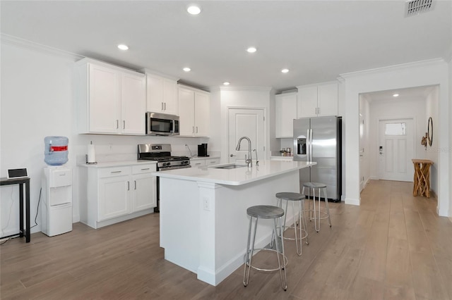 kitchen featuring white cabinets, a breakfast bar area, stainless steel appliances, an island with sink, and sink