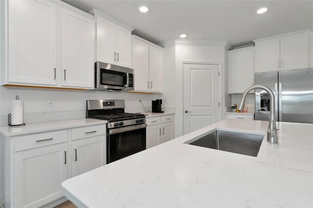 kitchen with white cabinets, appliances with stainless steel finishes, light stone countertops, and sink