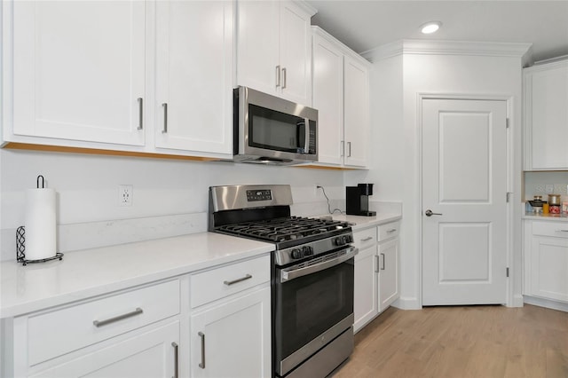 kitchen with stainless steel appliances, white cabinetry, crown molding, and light hardwood / wood-style flooring