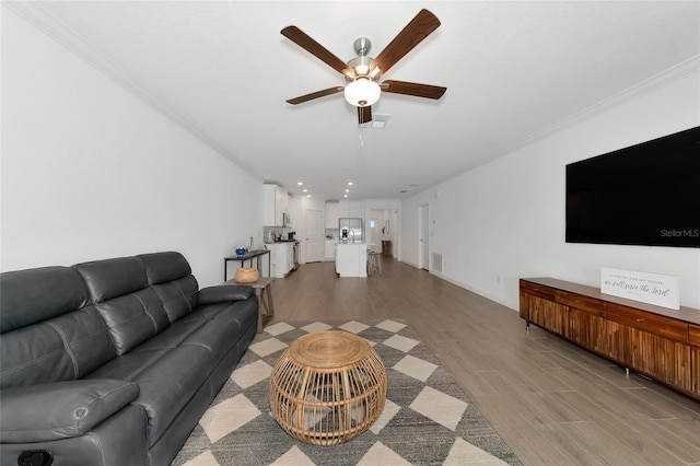 living room featuring ornamental molding, ceiling fan, and light wood-type flooring