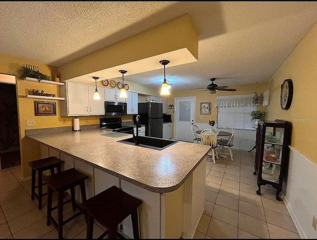 kitchen with a breakfast bar, black appliances, white cabinets, decorative light fixtures, and kitchen peninsula