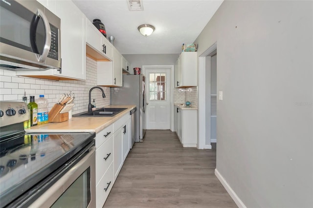 kitchen with tasteful backsplash, light wood-type flooring, white cabinetry, appliances with stainless steel finishes, and sink