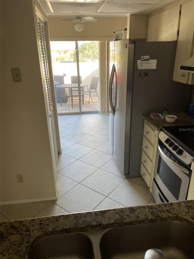 kitchen featuring dark stone counters, ceiling fan, light tile patterned floors, cream cabinets, and range with electric stovetop