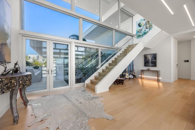 living room featuring a wealth of natural light, a towering ceiling, hardwood / wood-style floors, and french doors