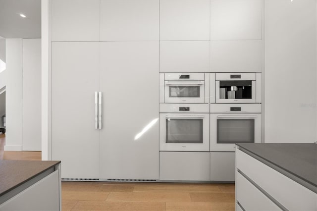 kitchen featuring white cabinetry, light wood-type flooring, and white double oven