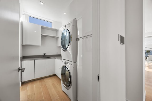 washroom featuring cabinets, stacked washing maching and dryer, sink, and light hardwood / wood-style flooring