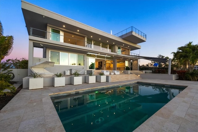 back house at dusk featuring a balcony and a patio