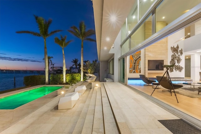 pool at dusk featuring a water view, a fireplace, and a patio area