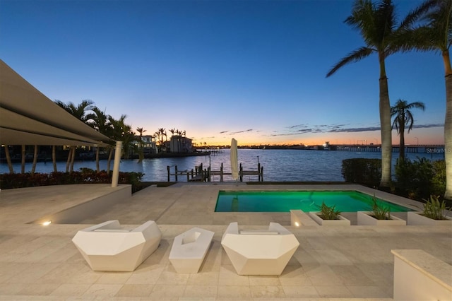 pool at dusk featuring a dock, a patio area, and a water view