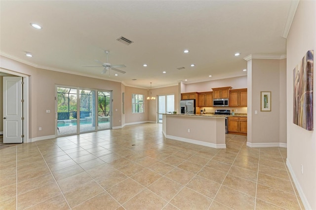 kitchen featuring light tile patterned floors, crown molding, appliances with stainless steel finishes, a kitchen island with sink, and ceiling fan with notable chandelier