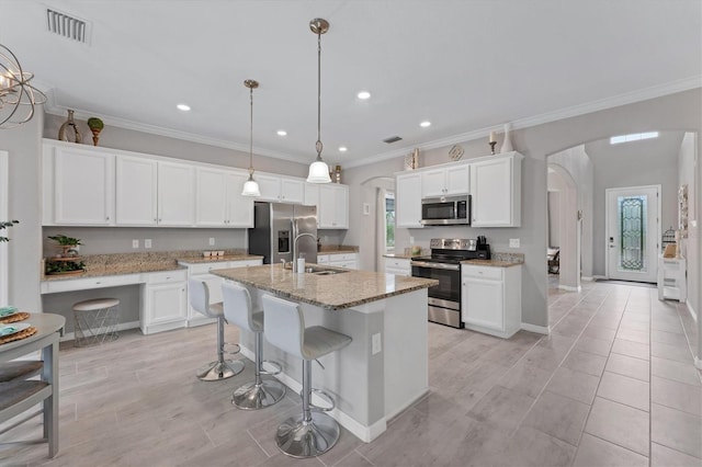 kitchen with appliances with stainless steel finishes, a kitchen island with sink, hanging light fixtures, white cabinets, and sink