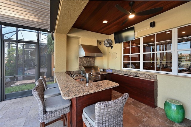 view of patio with an outdoor kitchen, exterior bar, ceiling fan, glass enclosure, and a grill