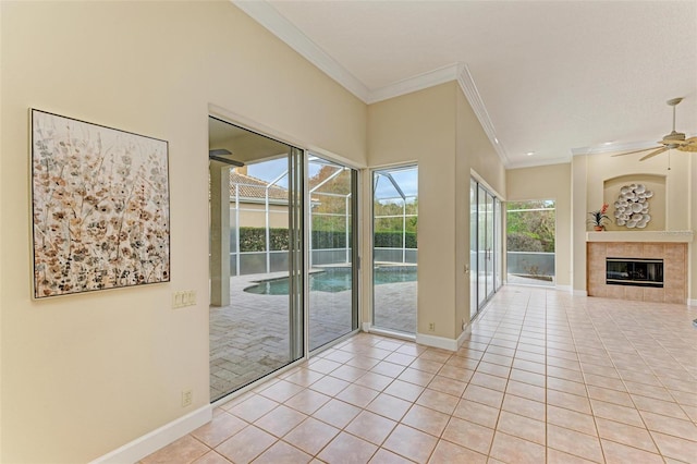 interior space with a tiled fireplace, light tile patterned flooring, ceiling fan, and crown molding