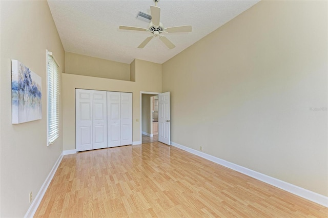 unfurnished bedroom featuring lofted ceiling, light wood-type flooring, ceiling fan, a textured ceiling, and a closet