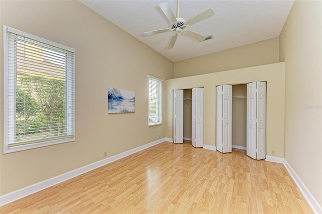 unfurnished bedroom with ceiling fan, a textured ceiling, multiple closets, and light wood-type flooring