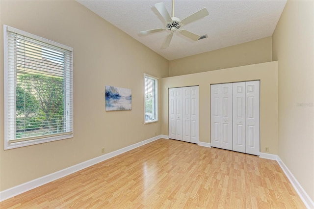 unfurnished bedroom with multiple closets, ceiling fan, a textured ceiling, and light hardwood / wood-style flooring