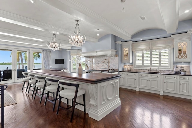 kitchen with tasteful backsplash, custom exhaust hood, sink, white cabinetry, and a kitchen island with sink