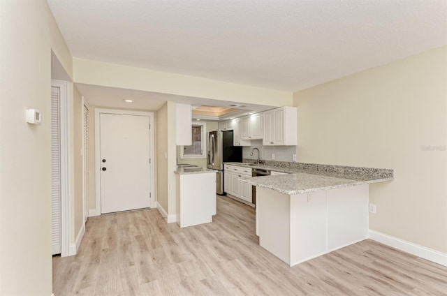 kitchen with kitchen peninsula, stainless steel fridge, light wood-type flooring, decorative backsplash, and white cabinetry