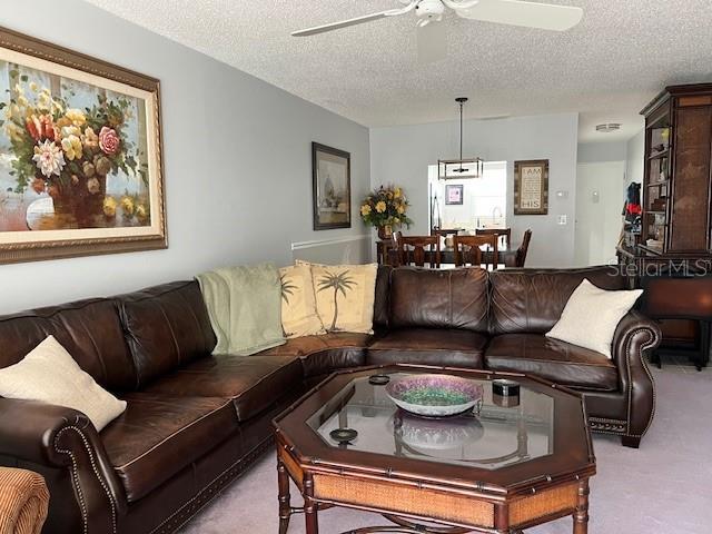 living room with light carpet, ceiling fan, and a textured ceiling