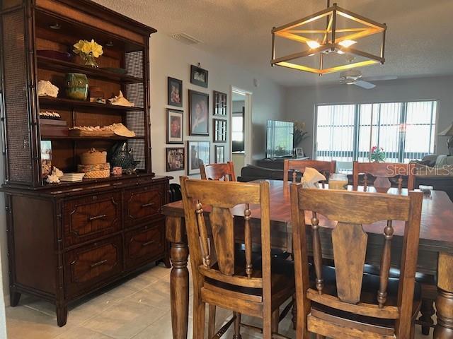 dining room with ceiling fan with notable chandelier, light tile patterned floors, and a textured ceiling