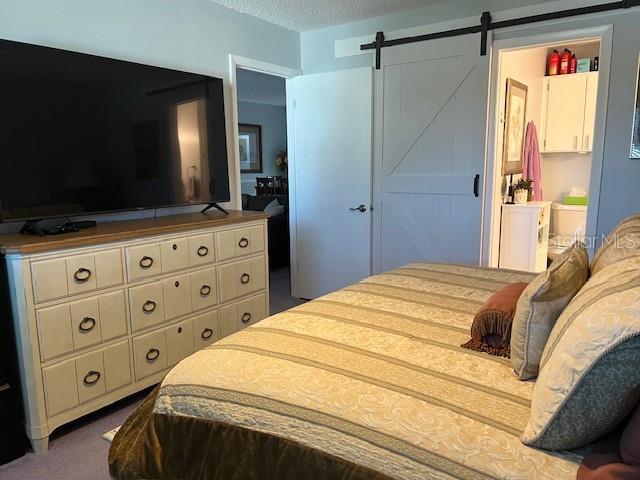 carpeted bedroom with a textured ceiling, a barn door, and connected bathroom