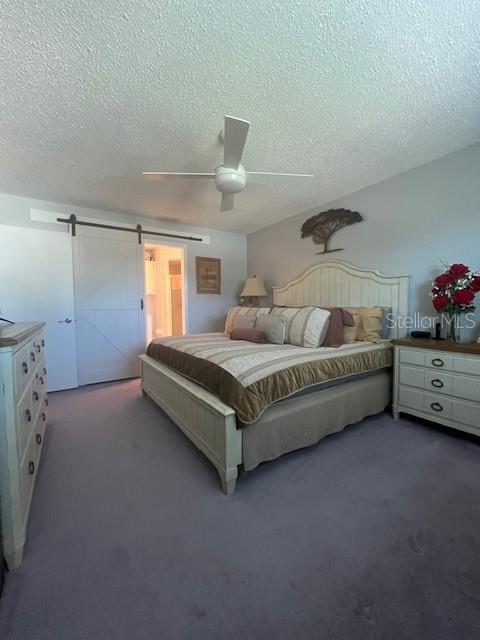 bedroom with a barn door, ceiling fan, and a textured ceiling