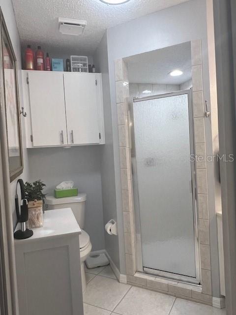 bathroom with vanity, a textured ceiling, tile patterned flooring, toilet, and a shower with shower door