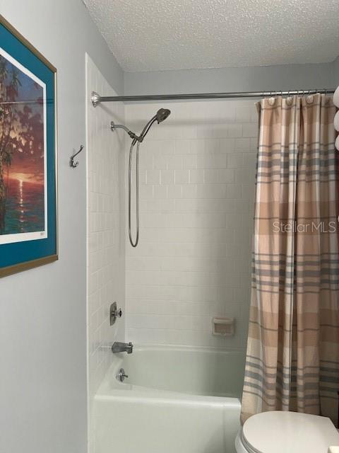 bathroom featuring shower / bath combination with curtain, toilet, and a textured ceiling