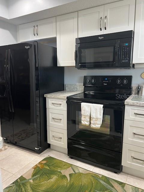 kitchen featuring white cabinets, light stone counters, light tile patterned flooring, and black appliances