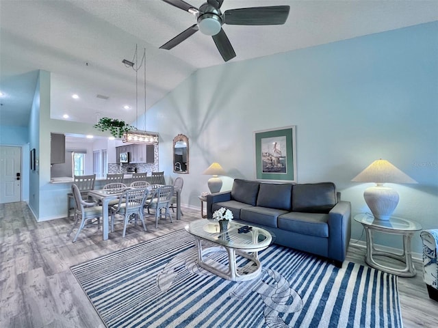 living room featuring a textured ceiling, light hardwood / wood-style floors, vaulted ceiling, and ceiling fan