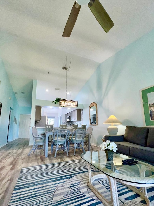 living room with ceiling fan, wood-type flooring, and vaulted ceiling