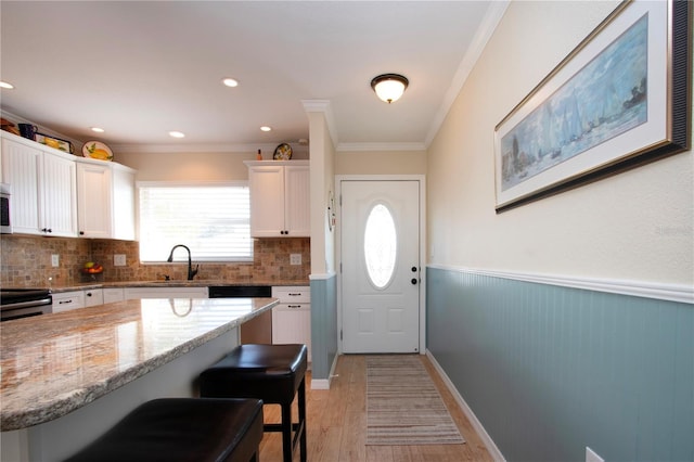 kitchen featuring sink, light hardwood / wood-style flooring, crown molding, a breakfast bar area, and white cabinets