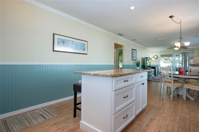 kitchen featuring light stone countertops, light wood-type flooring, a kitchen island, crown molding, and white cabinetry