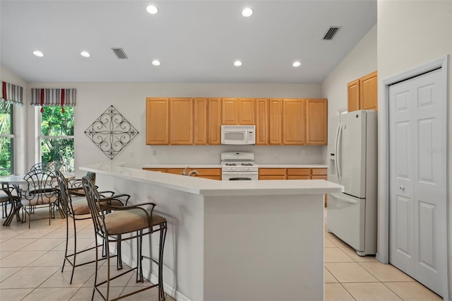 kitchen featuring white appliances, a center island with sink, light tile patterned floors, lofted ceiling, and a breakfast bar area