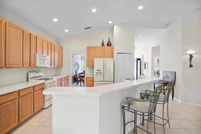 kitchen with white appliances, a kitchen breakfast bar, washing machine and dryer, light tile patterned floors, and lofted ceiling