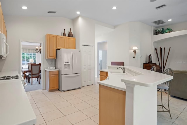 kitchen featuring sink, white appliances, a kitchen breakfast bar, an island with sink, and light brown cabinetry