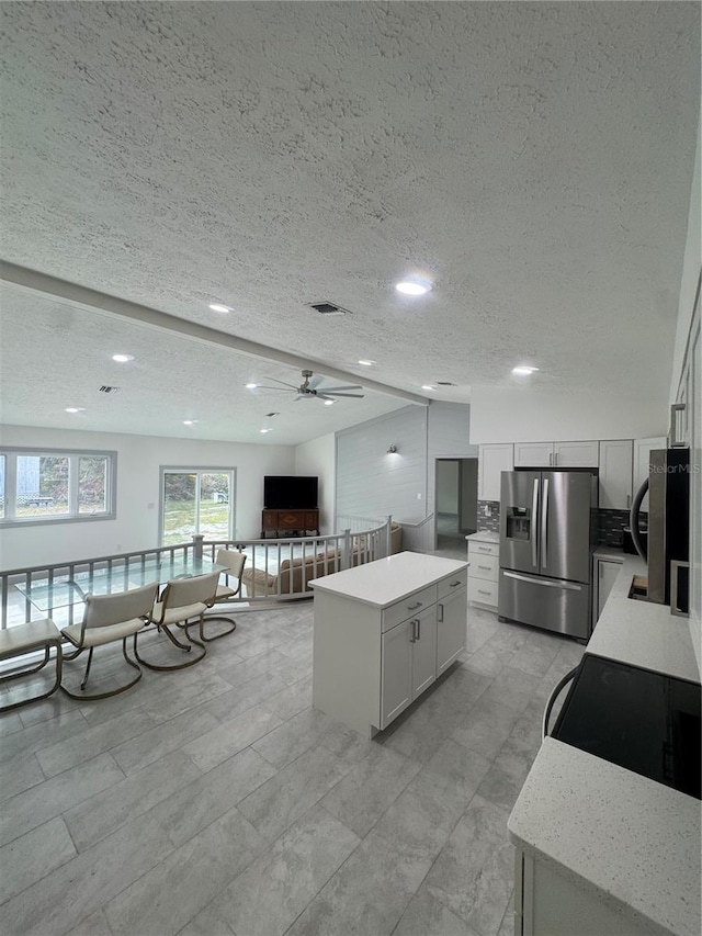 kitchen featuring stainless steel refrigerator with ice dispenser, a center island, white cabinetry, and ceiling fan