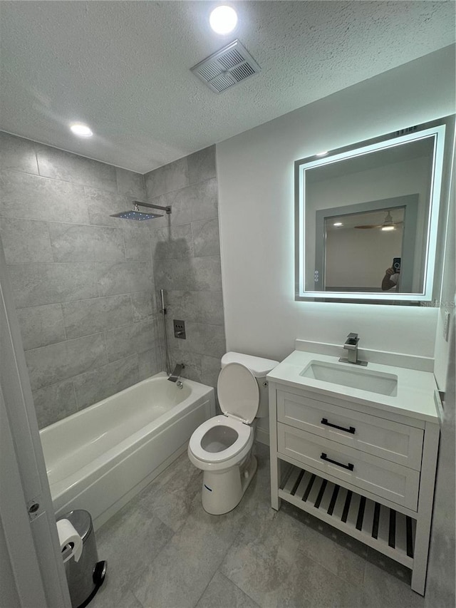 full bathroom featuring a textured ceiling, vanity, toilet, and tiled shower / bath