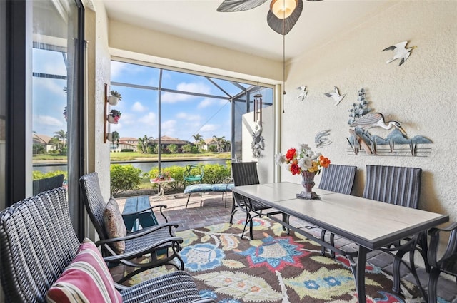 sunroom with ceiling fan and a water view