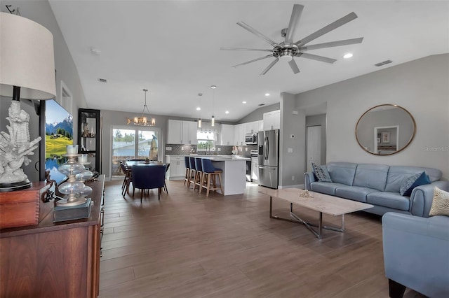 living room with ceiling fan with notable chandelier, wood-type flooring, and vaulted ceiling