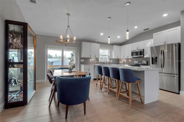 kitchen featuring stainless steel appliances, vaulted ceiling, a center island, white cabinetry, and hanging light fixtures