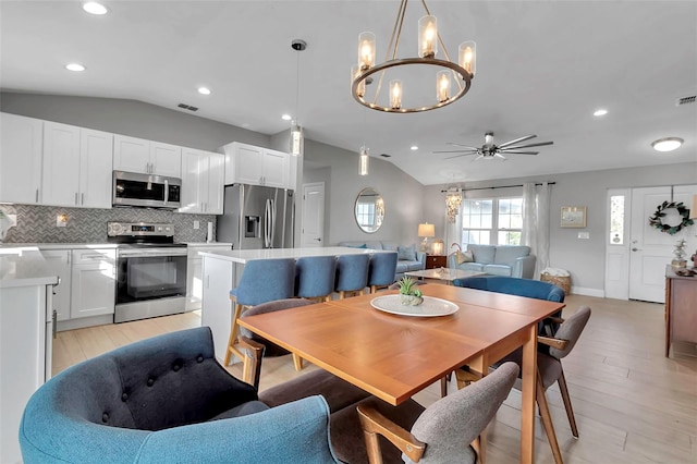 dining room featuring ceiling fan with notable chandelier, light hardwood / wood-style flooring, and vaulted ceiling