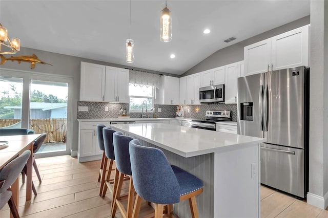 kitchen with a center island, white cabinetry, stainless steel appliances, and hanging light fixtures