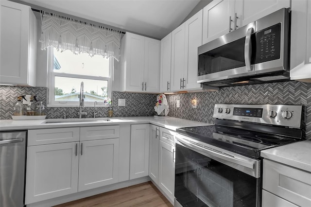 kitchen with backsplash, white cabinets, sink, vaulted ceiling, and appliances with stainless steel finishes