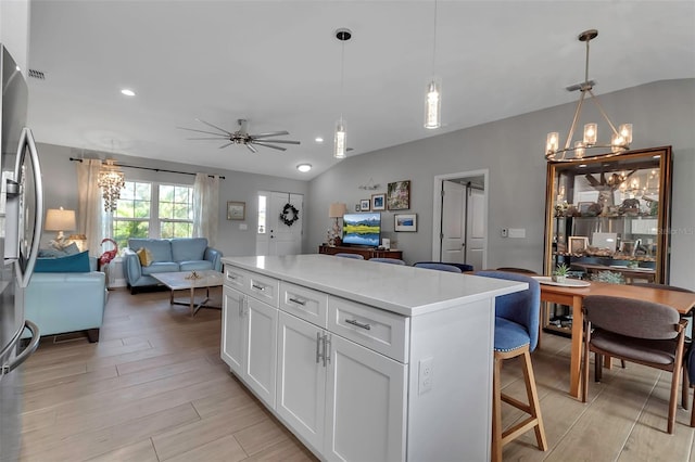 kitchen with white cabinetry, a center island, a kitchen breakfast bar, pendant lighting, and ceiling fan with notable chandelier