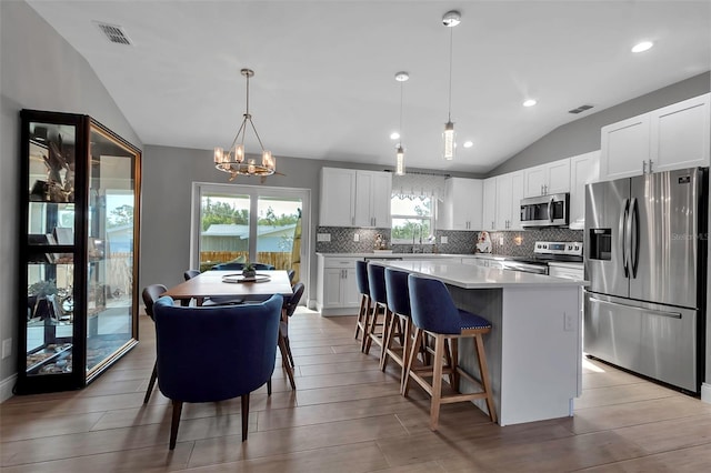 kitchen featuring a center island, vaulted ceiling, decorative light fixtures, white cabinetry, and stainless steel appliances